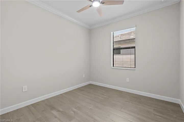 Unfurnished room featuring ceiling fan, crown molding, baseboards, and light wood-style flooring