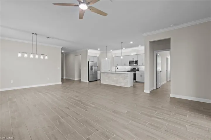 Unfurnished living room featuring a ceiling fan, baseboards, recessed lighting, light wood-type flooring, and crown molding