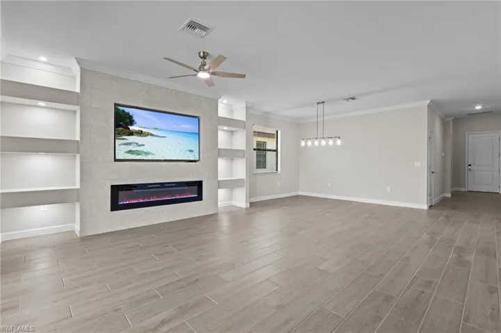 Unfurnished living room featuring baseboards, built in features, wood finished floors, a tiled fireplace, and a ceiling fan