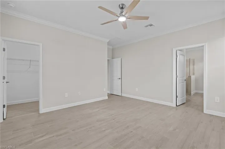 Unfurnished bedroom featuring ornamental molding, a spacious closet, light wood-style floors, baseboards, and a closet