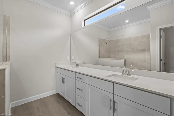 Full bath featuring wood finished floors, walk in shower, double vanity, ornamental molding, and baseboards