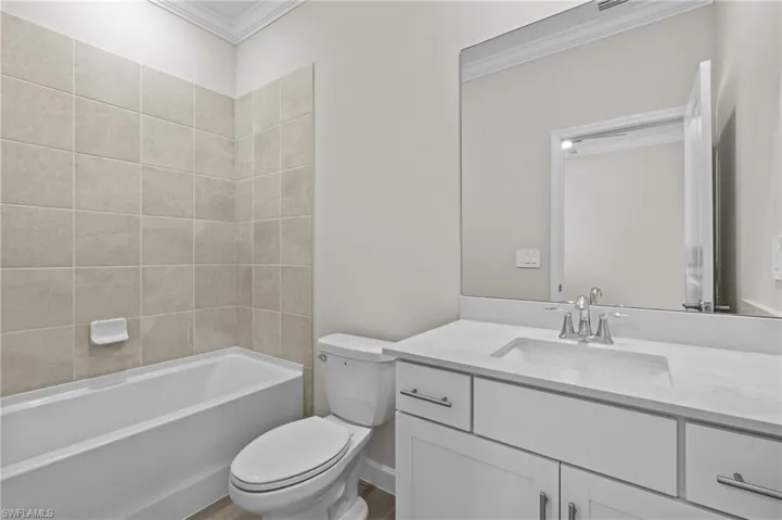 Full bath featuring ornamental molding, toilet, vanity, and washtub / shower combination