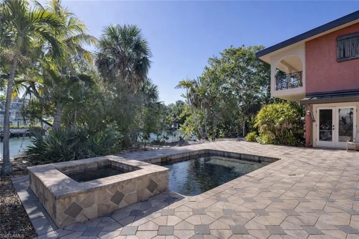 Combined pool / hot tub with a balcony, a patio area, and french doors
