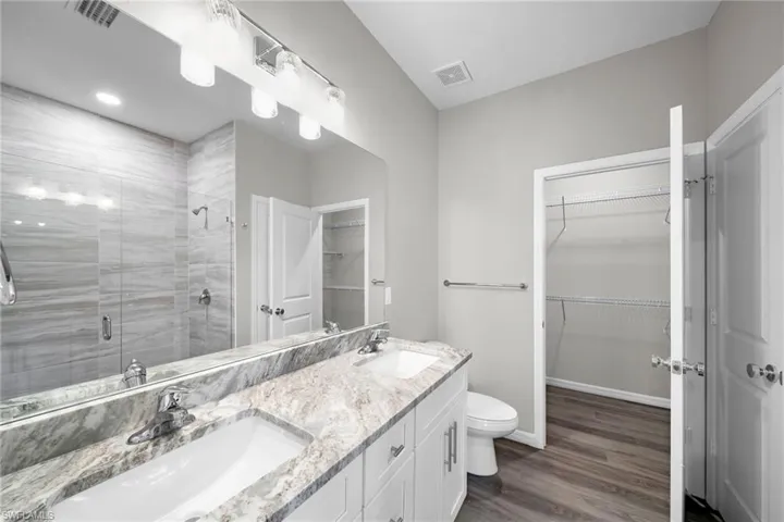 Bathroom featuring dual vanity, toilet, hardwood / wood-style flooring, and walk in shower