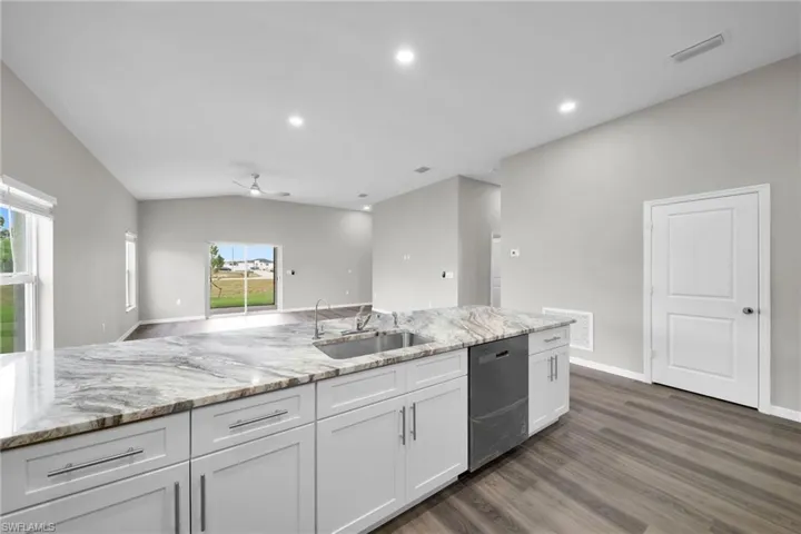 Kitchen with lofted ceiling, dishwashing machine, dark wood-type flooring, ceiling fan, and sink