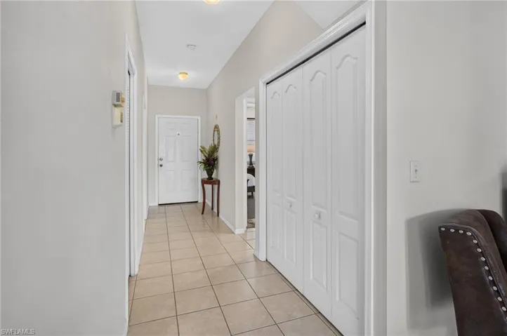 Entryway featuring neutral wall tones, square tile flooring, a white paneled front door, and a vaulted ceiling