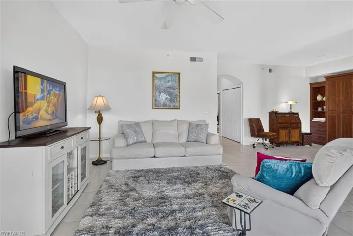 Spacious living area featuring light-toned tile flooring, high ceilings, and a ceiling fan