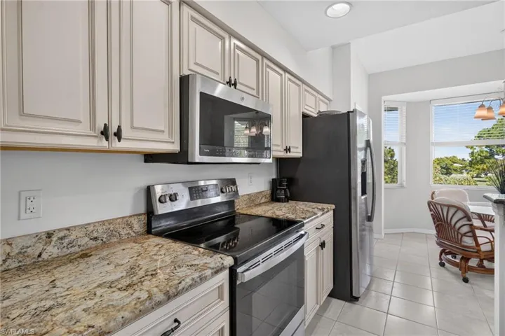 Kitchen featuring light-toned cabinetry, granite-finish countertops, stainless steel appliances, and tile flooring