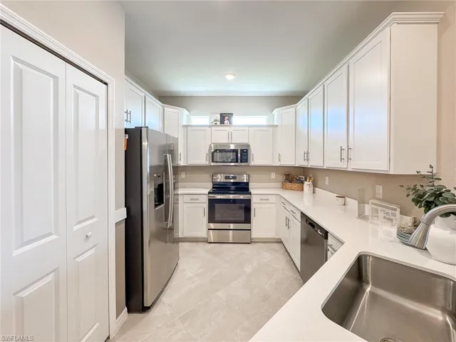 Kitchen with stainless steel appliances, white cabinets, light stone counters, and light tile patterned floors