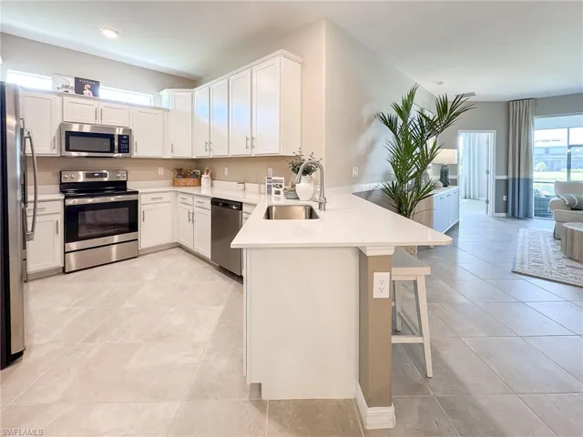 Kitchen with open floor plan, appliances with stainless steel finishes, white cabinetry, a peninsula, and a breakfast bar area