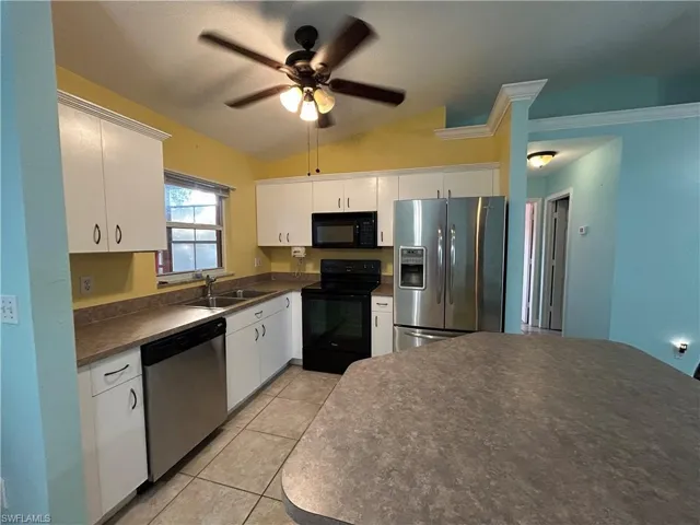 Kitchen with appliances, lofted ceiling, dark countertops, ceiling fan, and white cabinetry