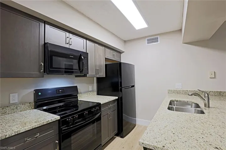 Kitchen with black appliances, light stone countertops, light wood-type flooring, and dark brown cabinetry
