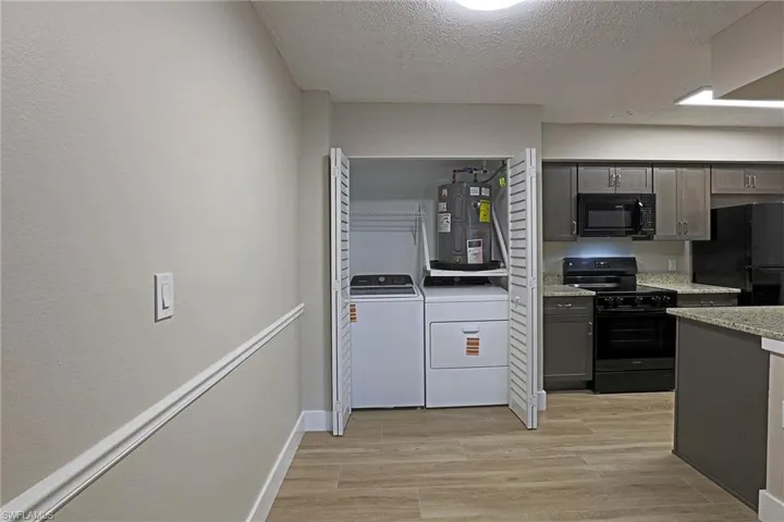 Kitchen with black appliances, light wood-style floors, a textured ceiling, water heater, and light stone countertops