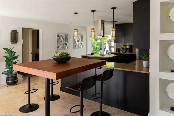 Kitchen featuring decorative light fixtures, a breakfast bar area, decorative backsplash, kitchen peninsula, and wall chimney exhaust hood