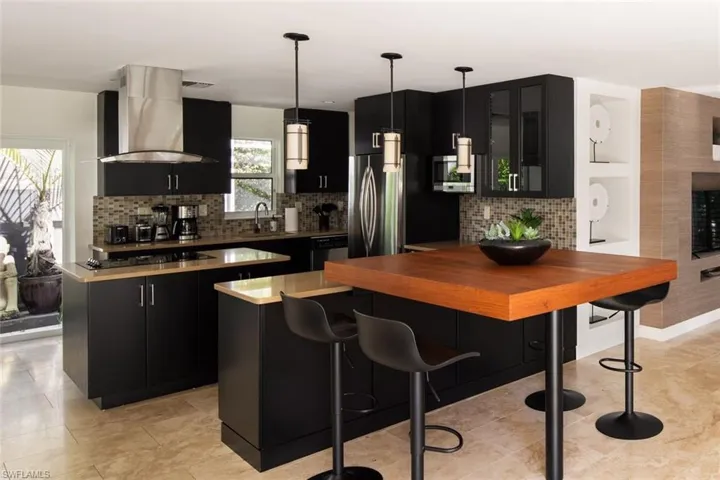 Kitchen with sink, exhaust hood, decorative light fixtures, a center island, and backsplash