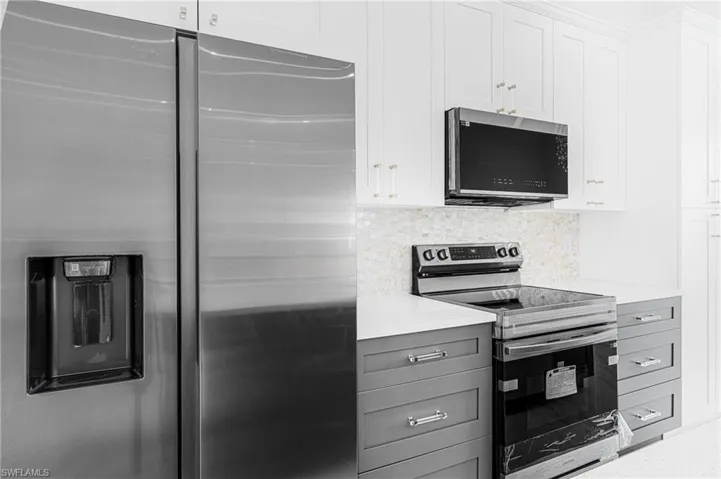 Kitchen featuring stainless steel appliances, gray cabinets, white cabinetry, and decorative backsplash