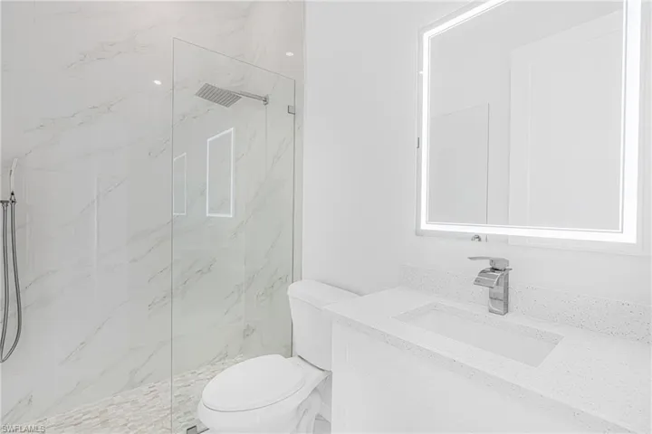 Full bath with toilet, a marble finish shower, and vanity