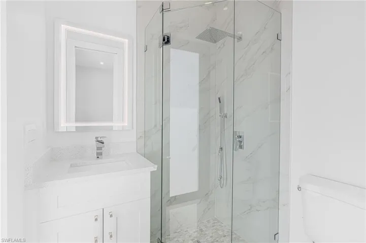 Bathroom with toilet, vanity, and a marble finish shower