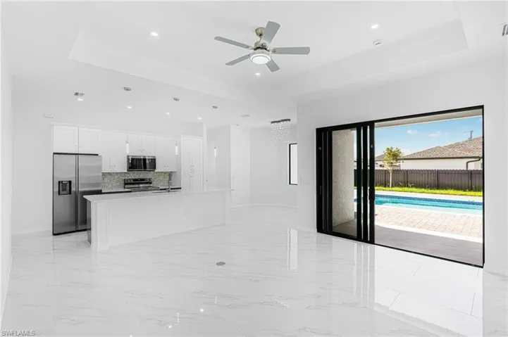 Kitchen featuring white cabinets, a raised ceiling, an island with sink, marble finish floor, and stainless steel appliances