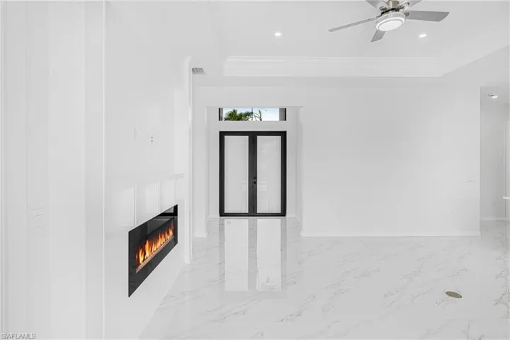 Unfurnished living room with a tray ceiling, french doors, marble finish floor, crown molding, and recessed lighting