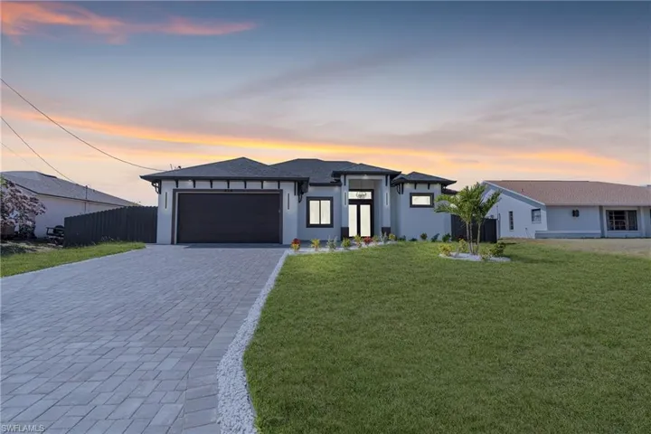 Prairie-style house featuring a garage, fence, a yard, decorative driveway, and stucco siding