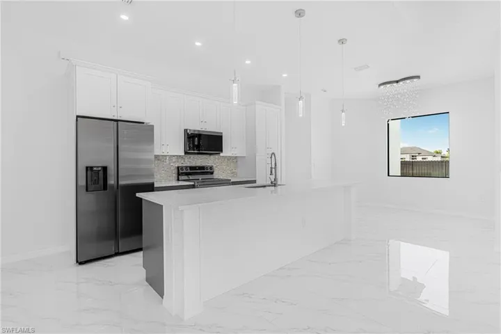 Kitchen with decorative backsplash, marble finish floor, stainless steel appliances, white cabinetry, and a sink