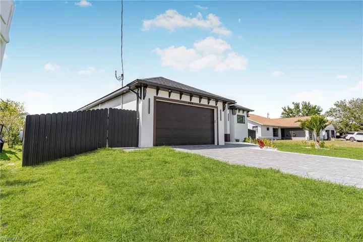 View of front of home featuring decorative driveway, stucco siding, fence, a garage, and a front lawn