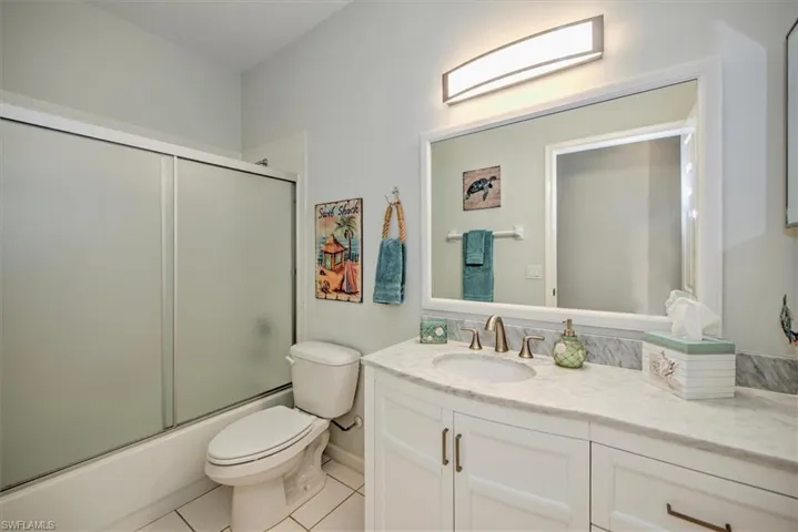 Full bathroom with bath / shower combo with glass door, toilet, vanity, and tile patterned flooring