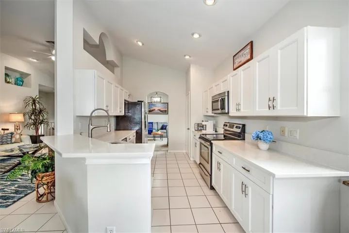 Kitchen with light tile patterned floors, white cabinetry, appliances with stainless steel finishes, and kitchen peninsula