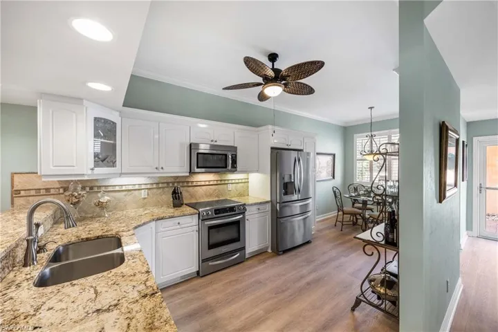 Kitchen with glass insert cabinets, stainless steel appliances, white cabinets, backsplash, and light stone countertops