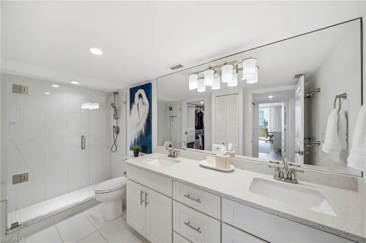 Renovated bathroom with double sinks, walk-in shower, and frameless glass door.