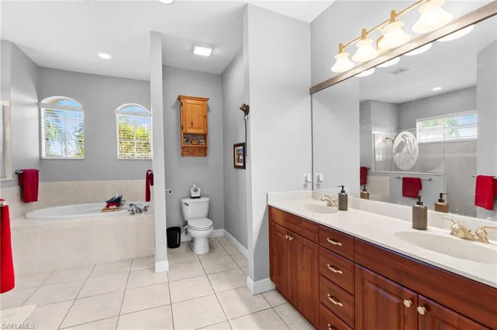 Bathroom with tile patterned flooring, vanity, toilet, and tiled bath