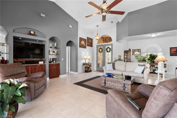 Tiled living room with built in shelves, ceiling fan, plenty of natural light, and high vaulted ceiling