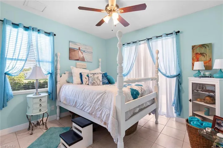 Guest bedroom Tiled bedroom featuring ceiling fan and multiple windows