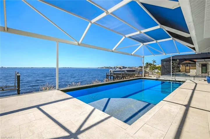 Outdoor pool with glass enclosure, a water view, a sunroom, a patio, and a dock