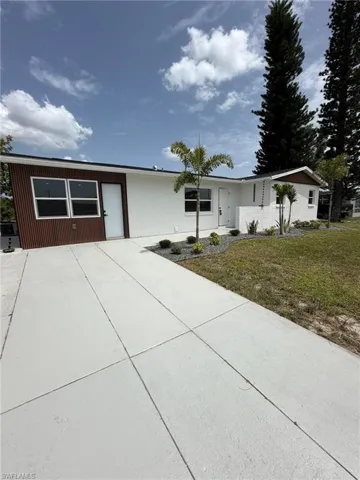 Exterior featuring white painted siding, a brown corrugated accent wall, a concrete driveway, and front landscaping