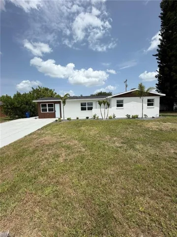 White exterior with brown trim, featuring multiple windows and a concrete driveway