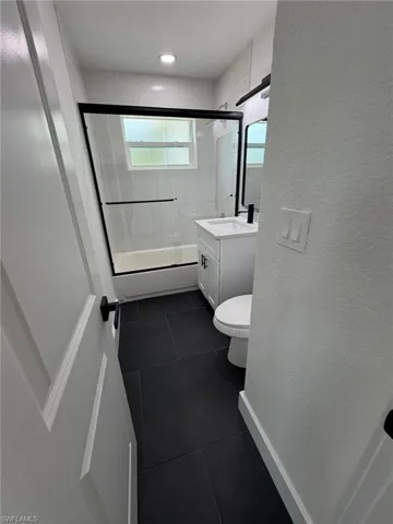 Black tile flooring with a white vanity featuring a black faucet and black cabinet hardware
