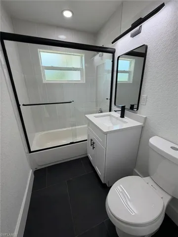 Bathroom featuring a white vanity with integrated sink, matte black fixtures, a framed mirror, and a shower-tub combination with a sliding glass enclosure