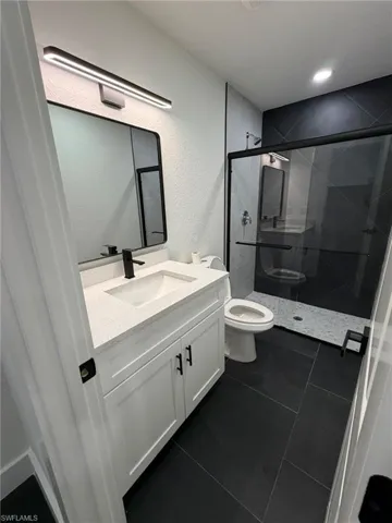 White vanity with quartz countertop, black hardware, black rectangular mirror, and a black-framed glass shower enclosure