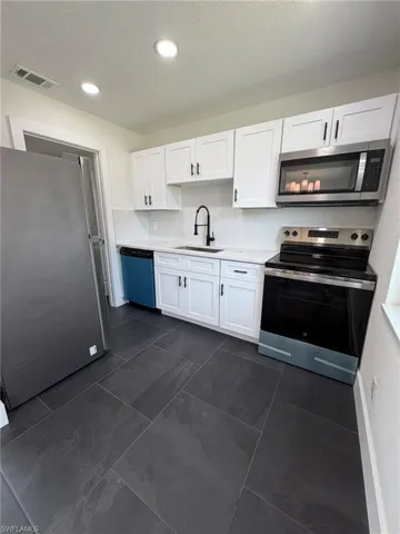 Kitchen featuring white shaker cabinetry, stainless steel appliances, a white tile backsplash, and dark tile flooring
