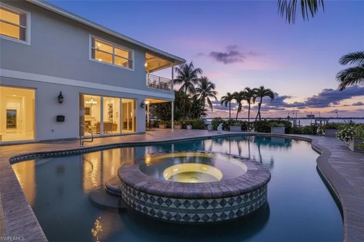 Pool at dusk featuring a balcony, a patio, and a pool with connected hot tub