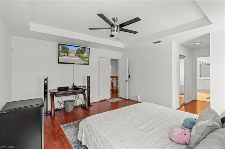 Bedroom with ceiling fan, a raised ceiling, and dark wood-type flooring