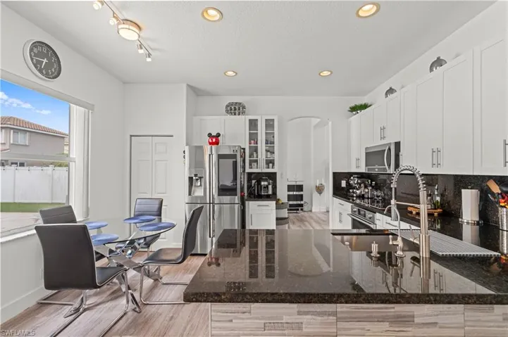 Kitchen with dark stone counters, stainless steel appliances, backsplash, rail lighting, and white cabinetry