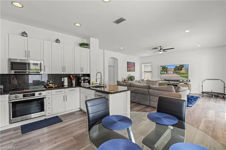 Kitchen with light wood-type flooring, white cabinets, backsplash, ceiling fan, and stainless steel appliances