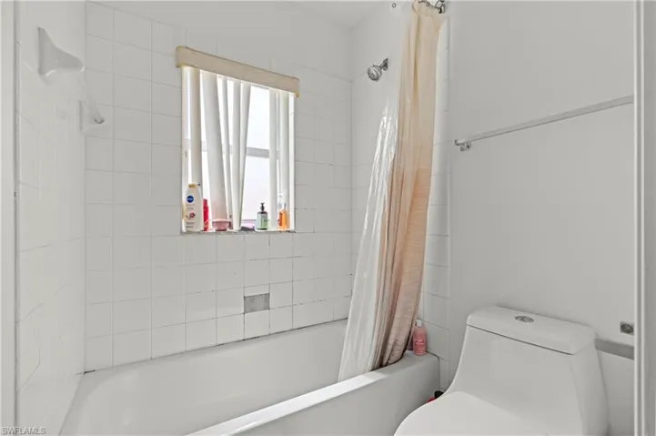 Bathroom featuring toilet and shower / bathtub combination with curtain