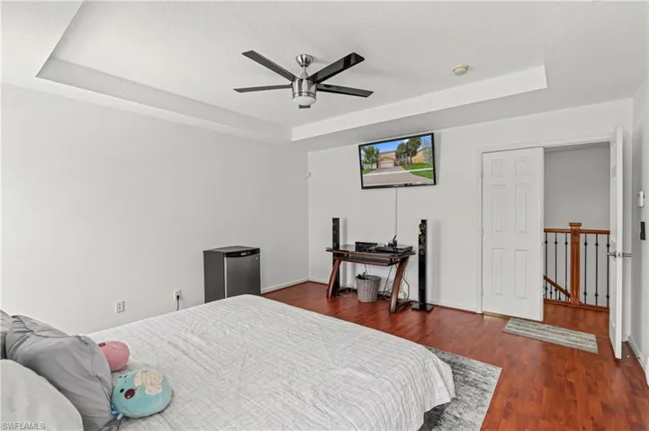 Bedroom featuring ceiling fan, dark hardwood / wood-style floors, and a tray ceiling