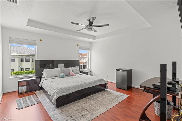 Bedroom with a textured ceiling, wood-type flooring, ceiling fan, and a tray ceiling