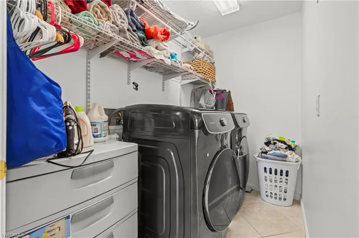 Washroom with light tile patterned flooring and washing machine and clothes dryer