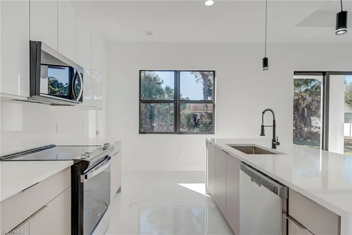 Kitchen with modern cabinets, stainless steel appliances, decorative light fixtures, and light stone countertops